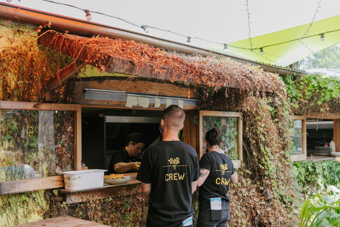 Two staff members waiting at the kitchen enveloped by green plants.