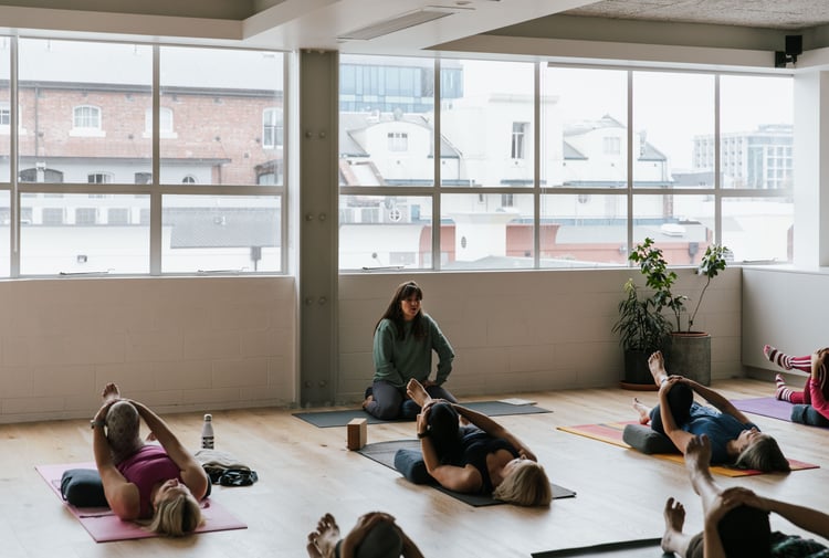 A yoga teacher taking a class of students lying on their backs.