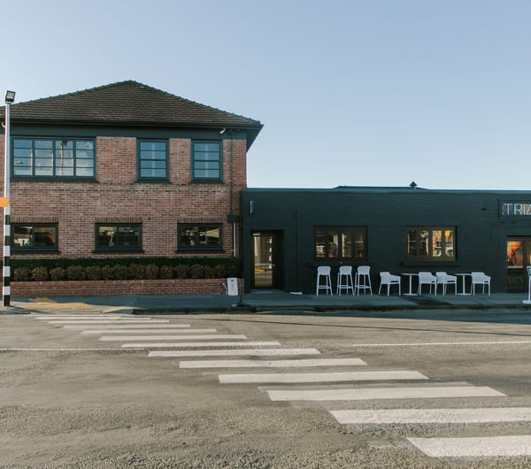 A view of a black and brick building from across the street on a sunny day.