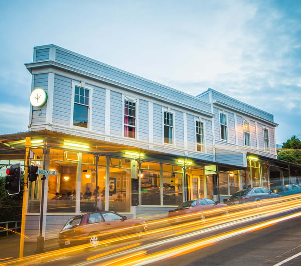 A photo of a blue building with cars whizzing by out front at dusk.