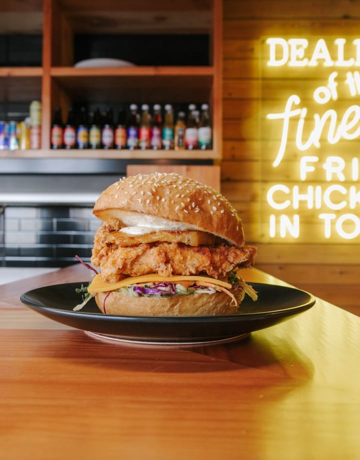 A Chicken burger on a black plate sitting on a wooden bench.