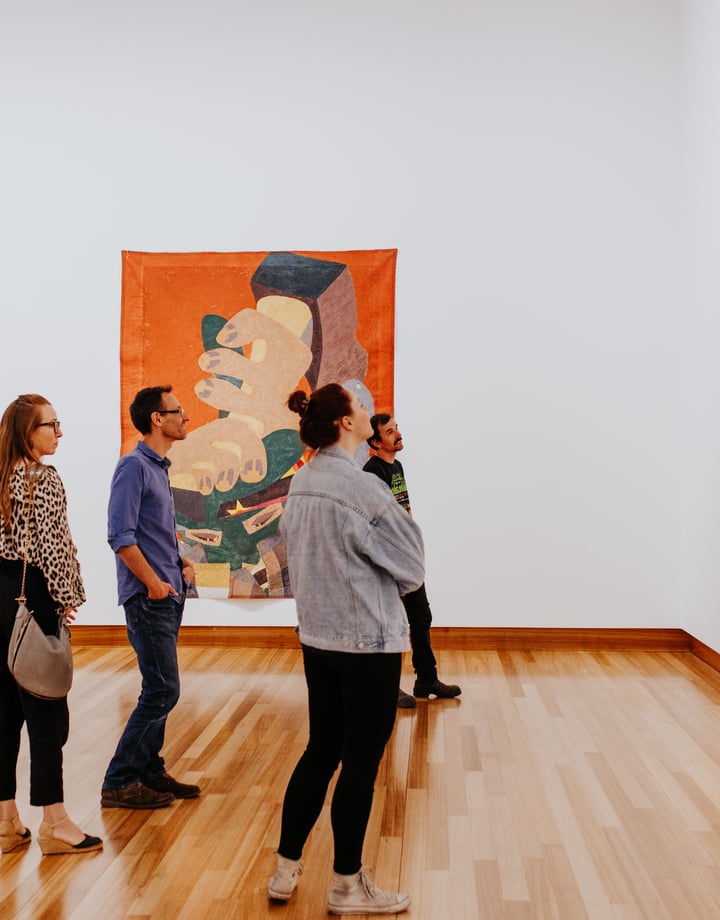 A group of adults looking intently at a colourful painting on a wall at Christchurch Art Gallery.