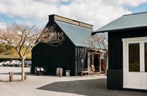 Two black barns outside in a sunny day.