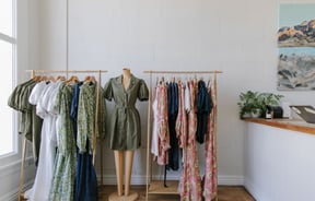 Colourful dresses and jumpsuits on a mannequin and on floating clothes racks.