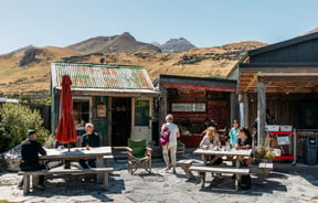 People dining outside next to old huts.