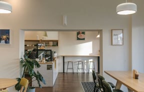 Interior of NOKI in Christchurch with wooden furnishings, green leather chairs, white-tiled countertop and framed art prints including someone sticking their finger in a fried egg