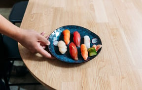 A hand holding a plate of sushi.