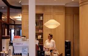 Wooden interior of Tosca in Remuera Auckland with smiling barista standing behind counter with coffee menu in background