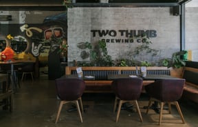 An indoor seating area with 'Two Thumb' printed on a brick wall.