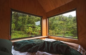 A cosy looking bed next to a window in a cabin.