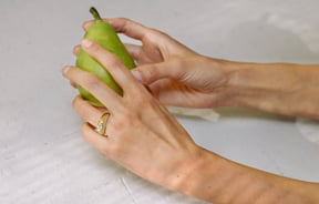 Two hands wearing rings holding a green pear.