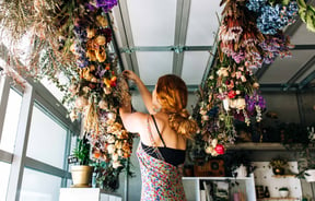 A woman working on bouquets hanging from the ceiling.