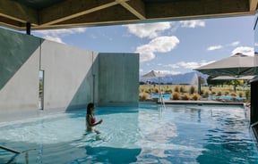 A woman walking through the water at Opuke Thermal pools with the Southern Alps in the background.