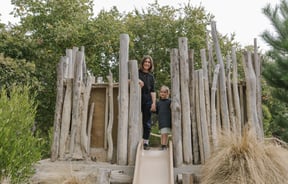 A woman and child standing amongst a log playground.