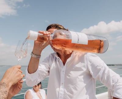 Man on boat in white shirt pouring a large bottle of rose with one hand