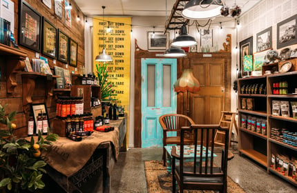 Interior of an artisan food shop with chilli oil on shelves, retro lampshades and antique chairs and table