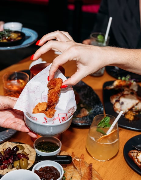 A hand reaching for a piece of fried chicken.
