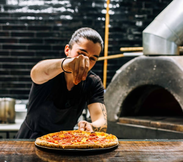 A chef making pizza next to a wood fire oven.