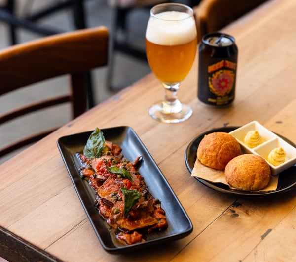 A meat dish and a bread dish and a glass of beer sit on a table at Atticus Finch.