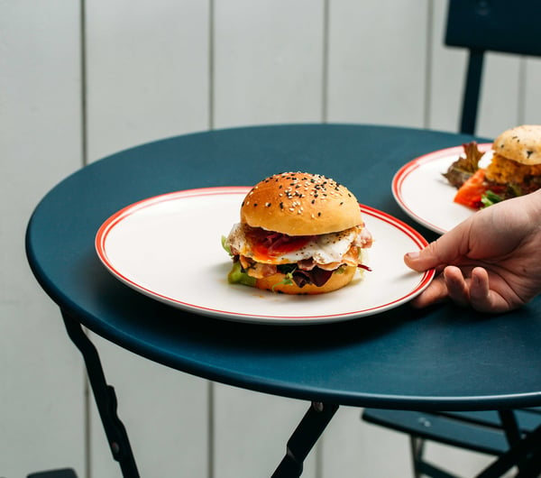 A hand putting a burger on a plate on to a blue table.