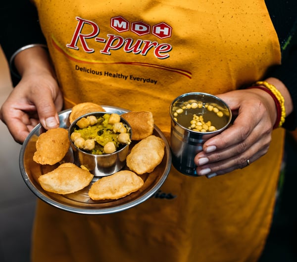A hand holding deep fried Indian food on a plate.