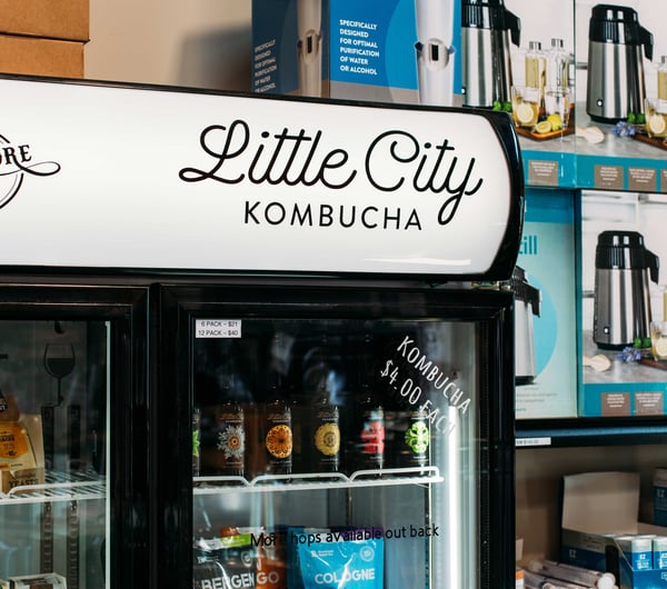A drinks fridge of with a black and white Little City Kombucha label.