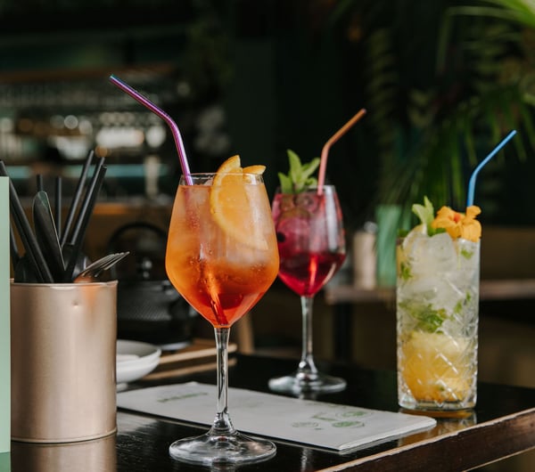 Three different cocktails on a black table with straws.