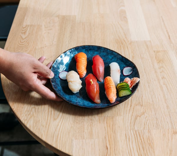 A hand holding a plate of sushi.