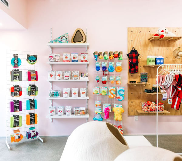 A pink wall with shelving units covered in colourful dog chew toys.