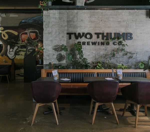 An indoor seating area with 'Two Thumb' printed on a brick wall.