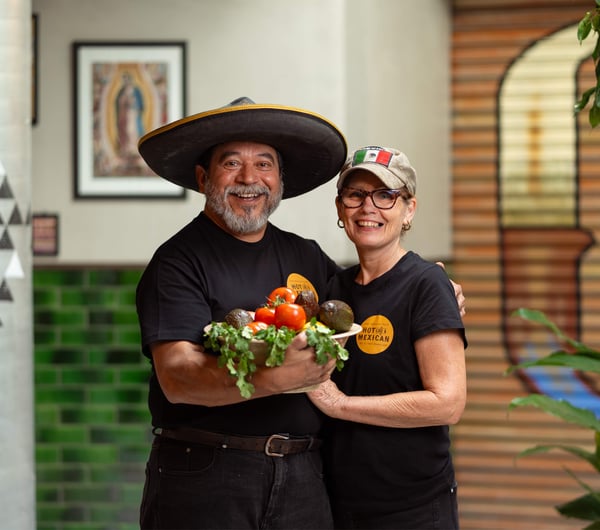 A man and woman holding a bowl of fresh vegetables smiling to camera.