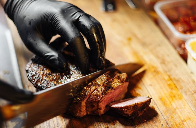 Close up of a gloved hand slicing red meat at 5th Street restaurant Christchurch.