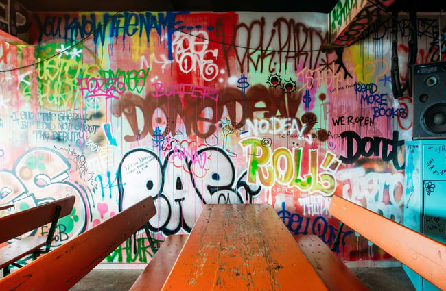 The colourful graffiti covered wall with long wooden tables next to the wall.