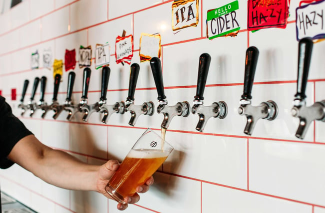 Someone pouring a drink from the taps on the white tiled wall with orange grout.