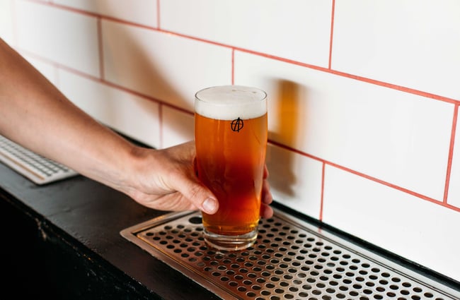 Someone grabbing a cup of beer from under the beer taps.