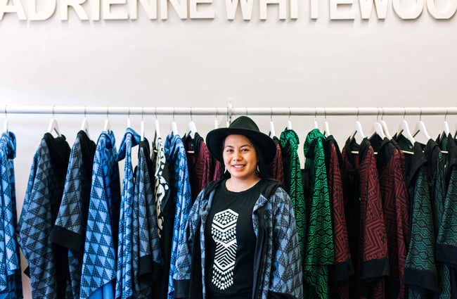 Adrienne Whitewood looking to camera in front of her clothes in her store.