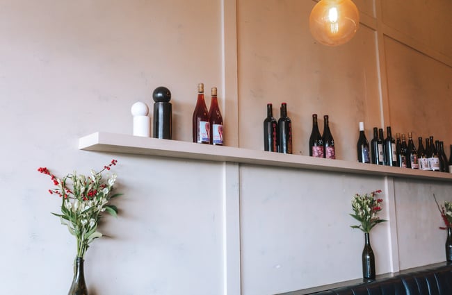 A white wall with vases and a shelf with bottles of wine.
