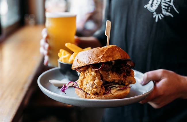 Hands holding a chicken burger and a beer.