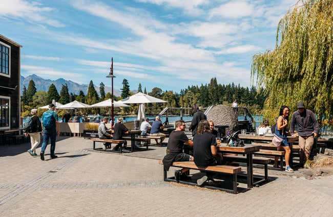 People dining outside by a lake on a sunny day.