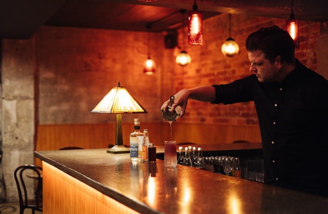 A bar man pouring a cocktail at the bar.