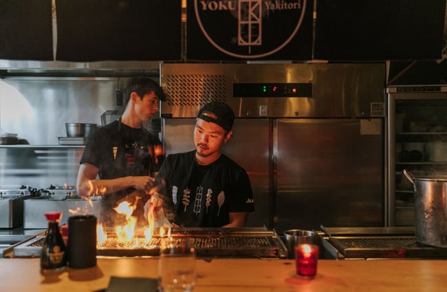 A chef working with flame behind in the kitchen.