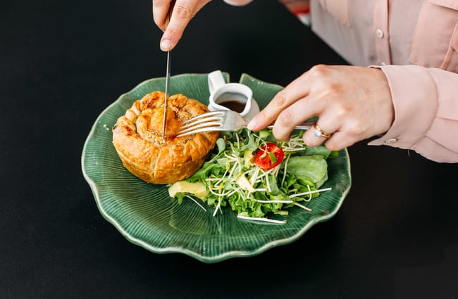 A pie and salad on a plate with a woman hovering a knife and fork over top.