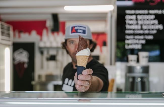 A man passing a waffle cone with chocolate and vanilla gelato across the counter.