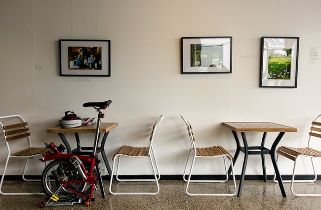 A unicycle next to empty tables and chairs against a large white wall.
