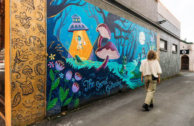 A woman walking past a painted mural of a secret garden.