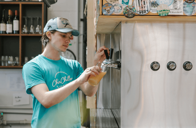 Someone in a blue t-shirt pouring a fresh brew from a silver and black tap.