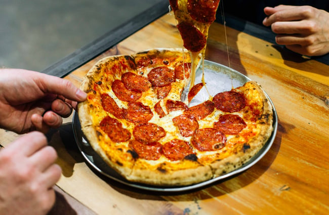 Close up of people pulling apart a pepperoni pizza.