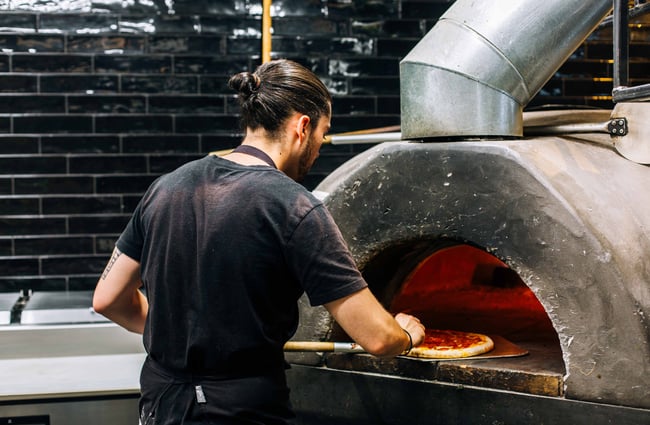 A man making pizza in a pizza oven.
