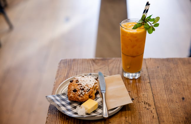 A glass of juice and sultana scone on a table.