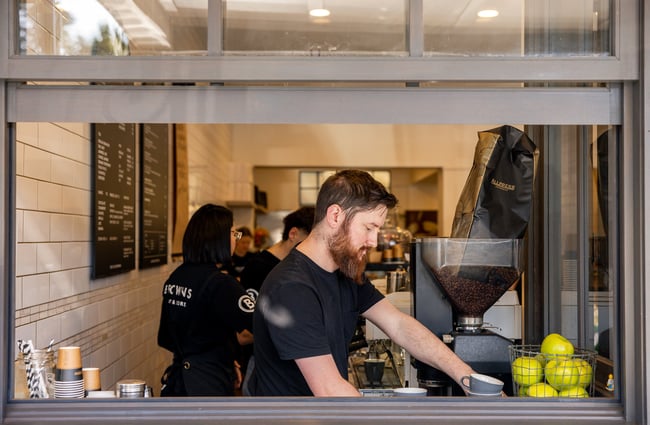 A staff member working inside a cafe window making coffee.